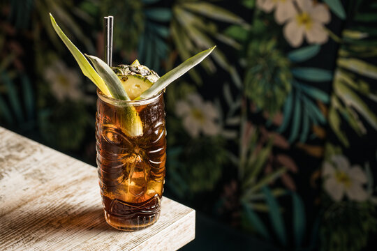 From above of glass tiki mug filled with alcohol beverage with straw decorated with fruit placed on edge of wooden table couch