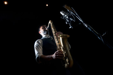 From below crop of male musician in classy outfit standing near microphone and playing alto saxophone during jazz concert
