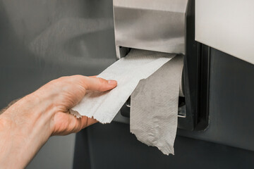 Man's hand takes or tears off toilet paper in a roll, close-up, soft focus