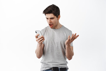 Frustrated man look confused at smartphone screen, read strange message on mobile phone and arguing, complaining, standing against white background
