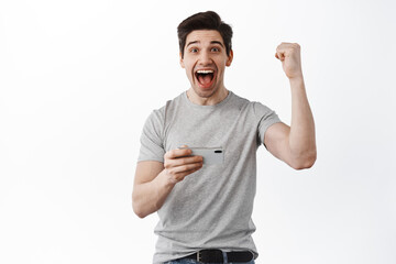 Excited guy celebrating after winning on smartphone, fist pump and scream yes joyful, triumphing of good news, standing against white background