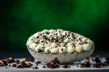 Stuffed white chocolate easter egg with broken cookies around on a white board. Gourmet. Green background.