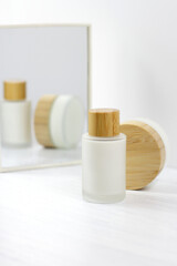 Glass matte cosmetic cream bottles with wooden top, eco cosmetics and mirror on white, lotion serum face body treatment
