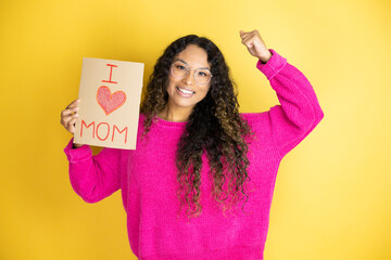 Beautiful woman celebrating mothers day holding poster love mom message very happy and excited making winner gesture with raised arms, smiling and screaming for success.