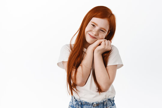 Adorable girl kid with ginger hair and freckles, lean on her little hands and smile cute, express love and care, admire something, standing dreamy against white background