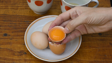Raw egg yolk separated inside half of broken eggshell holding in female fingers. Preparation of food ingredient for cooking ang baking. Retro kitchen crockery on background
