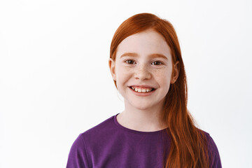Close up portrait of beautiful red haired girl with freckles, smiling with teeth and looking happy at camera, positive emotion, joyful kid, white background