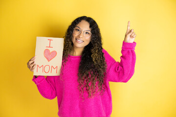 Beautiful woman celebrating mothers day holding poster love mom message smiling, looking at the camera and pointing up with finger and raised arm