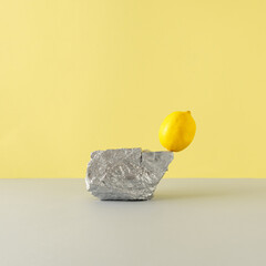 Abstract art composition with silver painted natural stone and yellow lemon fruit against bright yellow and gray background. Minimal food composition. Creative copy space.