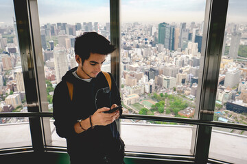 Young tourist guy in his phone with the panoramic view of Tokyo skyline, Japan