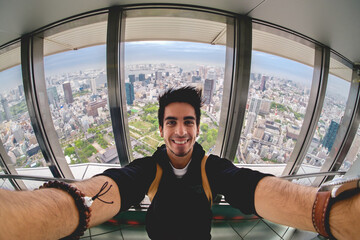 Young happy tourist guy taking a selfie with the panoramic view of Tokyo skyline, Japan