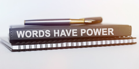 On the table are a notebook, a pen and a book. The book says - WORDS HAVE POWER