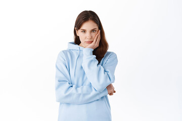 Sad and bored young woman student, lean head on hand and stare indifferent at camera, standing...