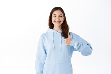 Very well, great choice, nice work. Smiling young woman stay positive, encourage you, give praises or guarantee, showing thumbs up in approval, standing against white background