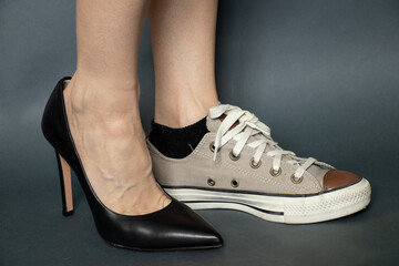 on one leg black high-heeled shoes on the other sport sneaker on the legs of a girl on an isolated...