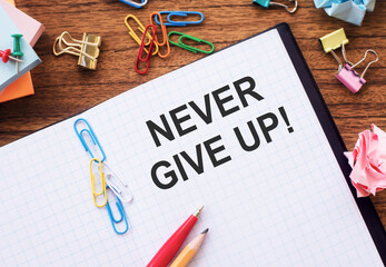 Notepad with the text NEVER GIVE UP on the table with colored paper clips and crumpled sheets.