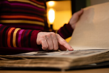 Elderly woman looks through an family album with old photos at table at home. Granny memories past times and remembering his life.