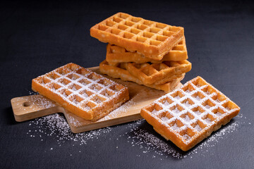 Sweet waffles sprinkled with powdered sugar prepared for serving. A tasty dessert eaten with fruit and preserves.