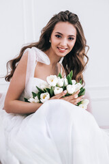 Bride in beautiful dress holding wedding bouquet and sitting on sofa indoors