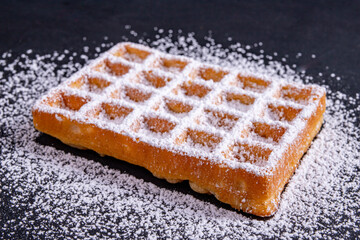 Sweet waffles sprinkled with powdered sugar prepared for serving. A tasty dessert eaten with fruit and preserves.