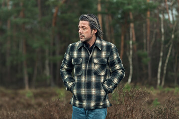 Man with stubble beard in a checkered coat in a rainy heathland.