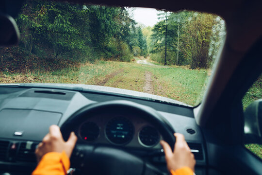 Driver Dressed Bright Orange Jacket Driving A Modern Off Road Right Hand Drive RHD Car On The Mountain Green Forest Country Road. POV Inside Car Windscreen View Point. Safely Auto Driving Concept.