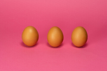 Three organic brown chicken eggs on pink background. Minimal Easter background