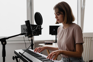 young woman recording a song playing piano and singing at home