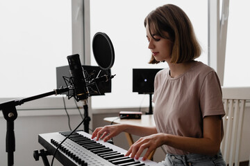 young woman recording a song playing piano and singing at home © Anastasia