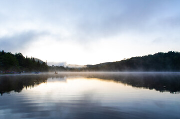 plan large d'un lac calme miroitant le ciel lors d'un lever de soleil brumeux