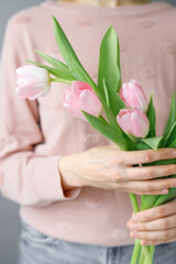 Obraz na płótnie Canvas pink tulips with green leaves in a glass vase, a woman holding tulips in her hands, florist, floristry, mother's day gift, bouquet for March 8, bouquet for a girl on her birthday, bouquet of tulips