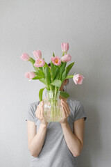 pink tulips with green leaves in a glass vase, a woman holding tulips in her hands, florist, floristry, mother's day gift, bouquet for March 8, bouquet for a girl on her birthday, bouquet of tulips