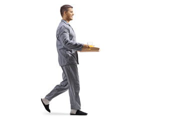 Full length profile shot of a man in pajamas walking and carrying a breakfast tray
