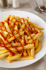Homemade French Fries with Ketchup, Salt and Pepper on a white plate on a white wooden background, low angle view. Close-up.