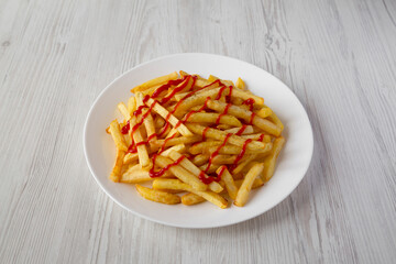 Homemade French Fries with Ketchup, Salt and Pepper on a white plate on a white wooden background, side view.