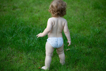 Back view of baby standing barefoot on the green lawn. Happy childhood and child healthcare. Kids growing.