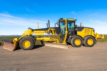 Motor grader in a road construction site in the countryside under blue sky  - obrazy, fototapety, plakaty