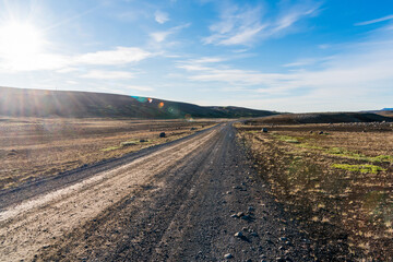 Fototapeta na wymiar Empty gravel road in a barren volcanic landscape in Iceland on a bright sunny summer day. Lens flare.