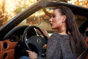Sexy young woman in jeans and in a grey sweater sits in a cabriolet