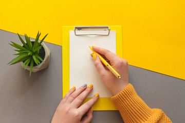 Female hands with fresh manicure writing on paper. Office table desk trendy yellow and grey colors....
