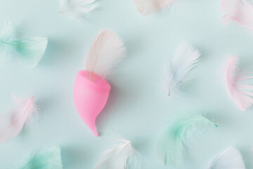 Menstrual cup and feathers on blue background. Top view, flat lay