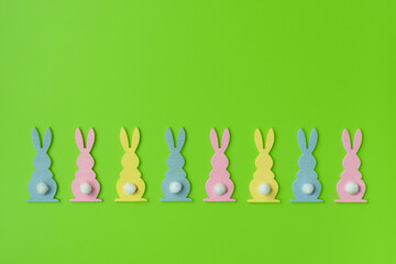 Easter Holiday minimal concept. Row of decorative multicolored easter bunnies isolated on green background. Creative flat lay. For design cards or web banners. Copy space