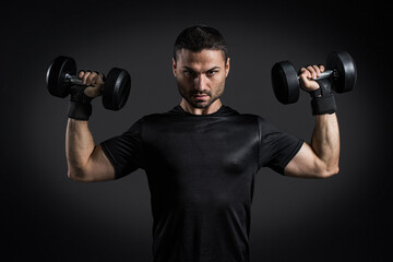 Naklejka na ściany i meble Young power athletic man doing exercise on biceps with heavy dumbbells in gym on black background. Strength and motivation.