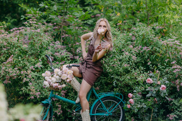 Elegant girl enjoys the fragrance of a flower with a bouquet of peonies on a bicycle in the park