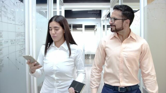 Pareja de hombre y mujer caminando por pasillo de oficinas con telefono movil