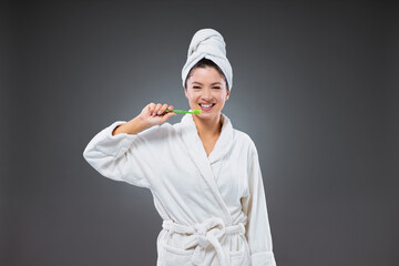 Tooth brushing and oral care.A smiling girl in a bathrobe and with a towel wrapped around her head after bathing, holding a toothbrush in her hand brushing her teeth