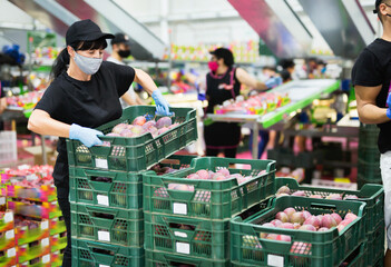 Focused diligent efficient serious glad female worker wearing protective face mask working at fruit warehouse carrying box with mangos