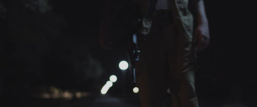 An adult soldier in uniform walking near a street light with a rifle at night.
