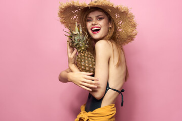 woman in beach hat pineapple exotic swimsuit pink background