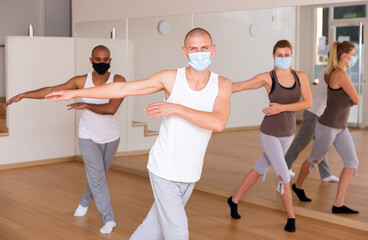 Obraz premium Portrait of man dancing during group workout in fitness center, all people wearing face masks and keeping social distance for viral protection